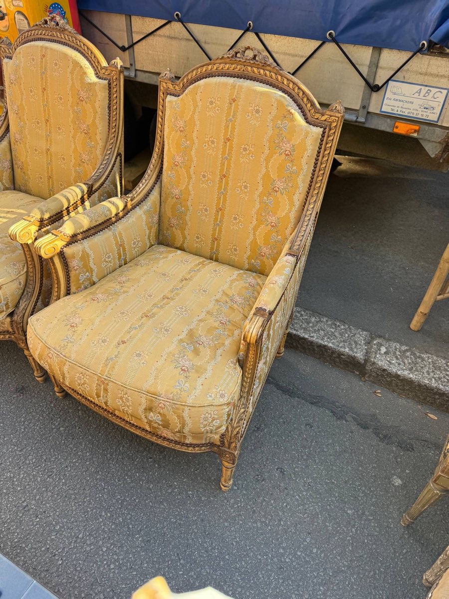 A pair of gilt Louis XVI-style bergere armchairs upholstered in yellow floral silk for sale at a French flea market stall