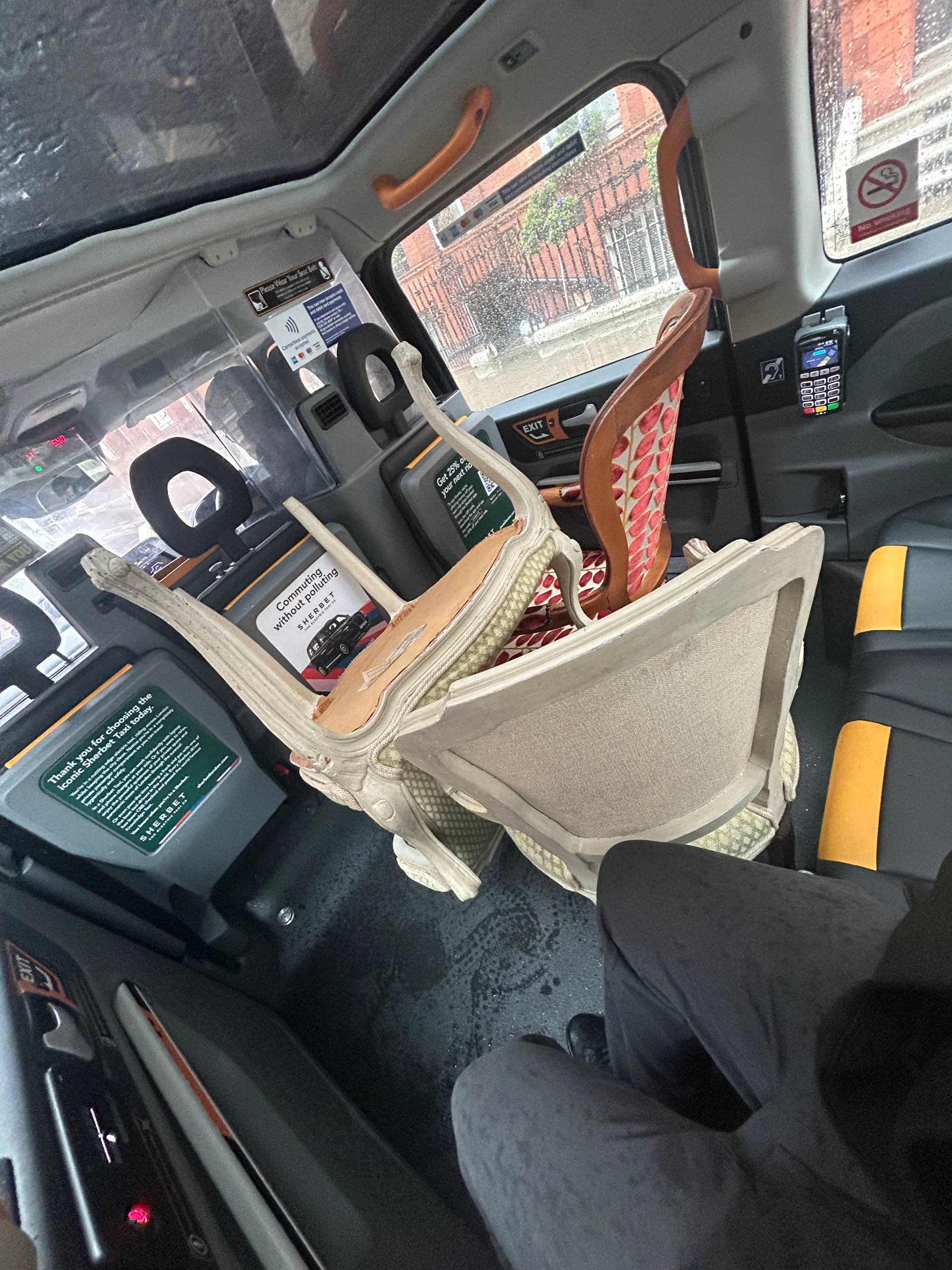 Vintage chairs squeezed into the back seat of a UK black cab — improvised reseller transport
